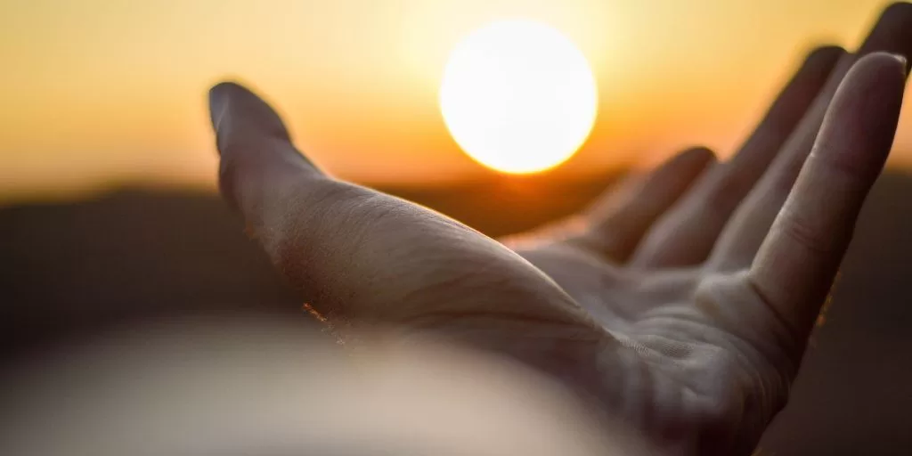 A man reaching toward the sun with his hand