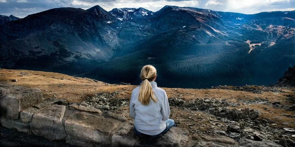 A woman seating on a wall and looking at the mountains to clear her mind