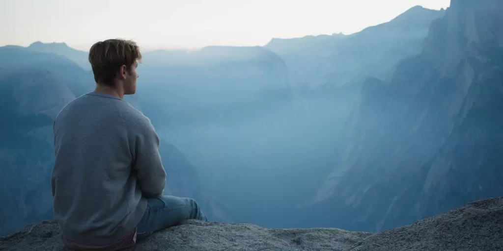 A wondering man sitting down and observing the mountains