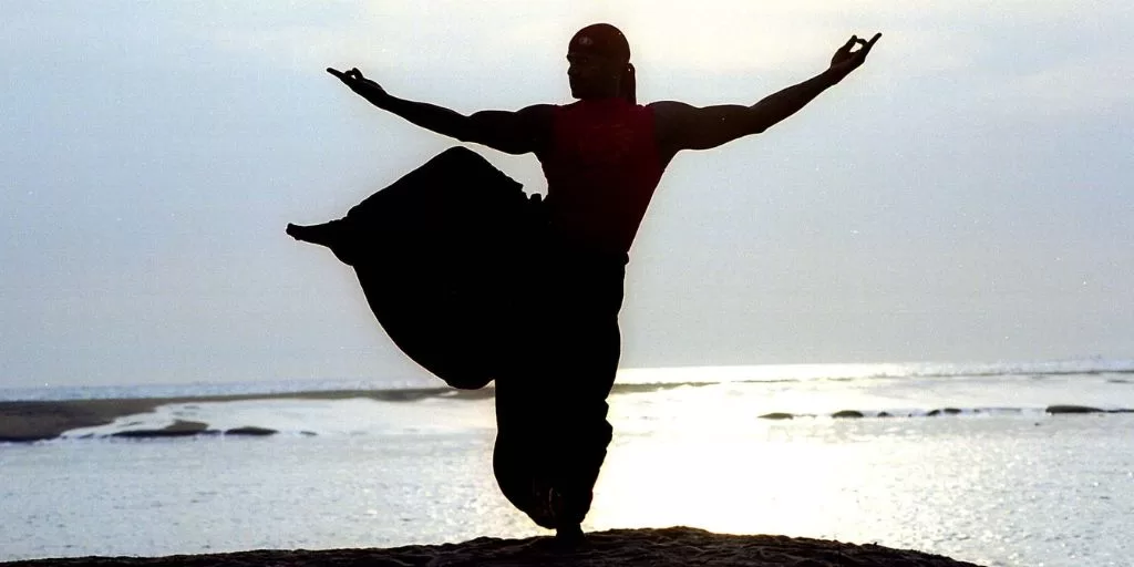 Muscular man balancing on one leg at a beach