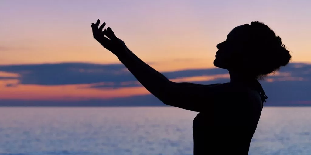 Happy woman by the sea lifting her arms toward the sun