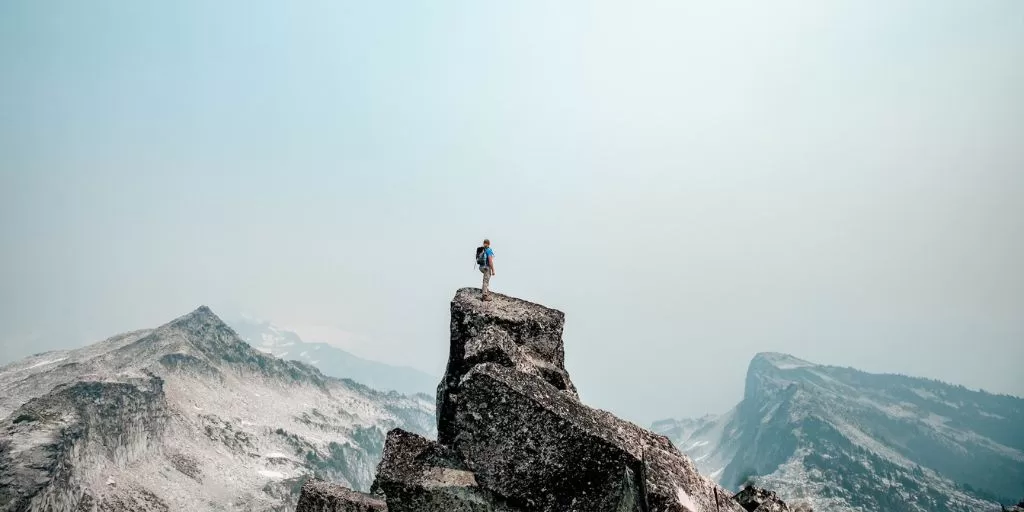 Victorious mindset: A hiker standing on a mountain peak looking down on the world