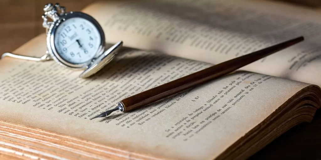 A vintage watch and a pen lying on top of an open old book