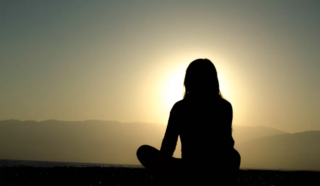 A woman meditating at the sunset and setting new mental health goals for herself