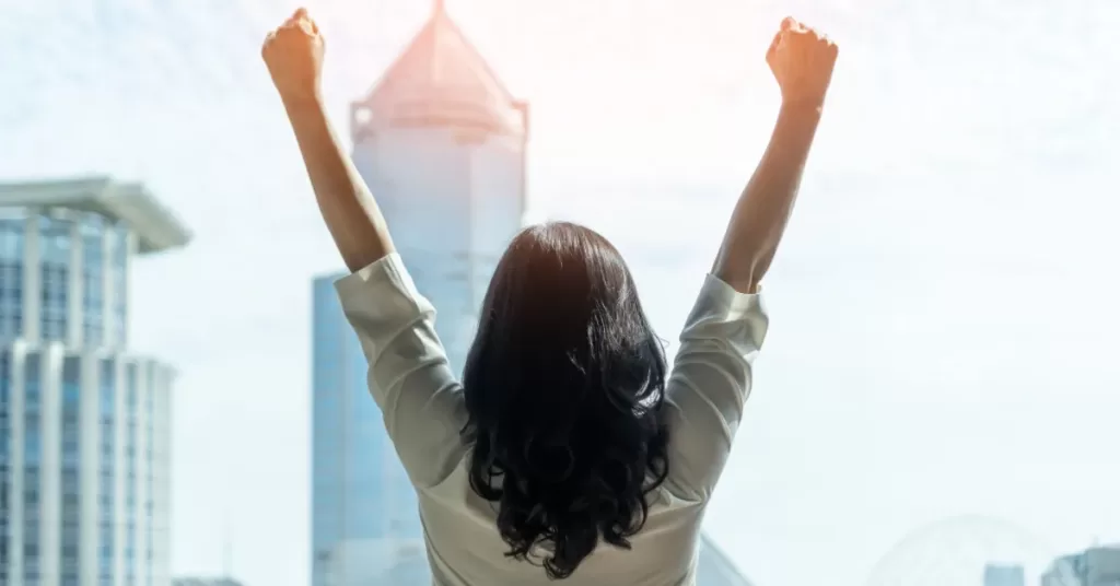 Self-confident and successful woman raising her arms up