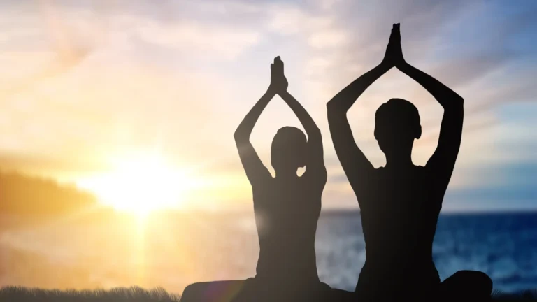 Silhouettes of 2 people meditating at sunset and releasing their negative emotions