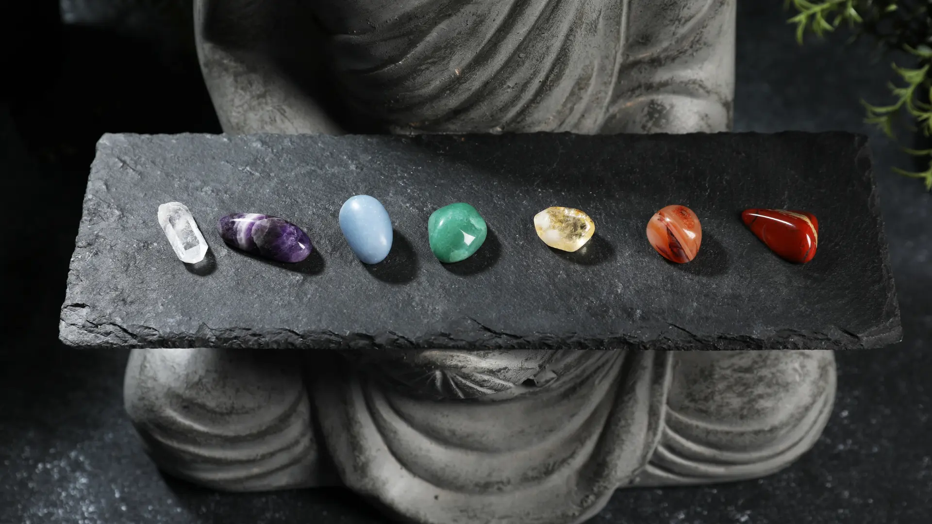 Buddha statue holding a board with 7 crystals, each representing a specific chakra from Muladhara to Sahasrara
